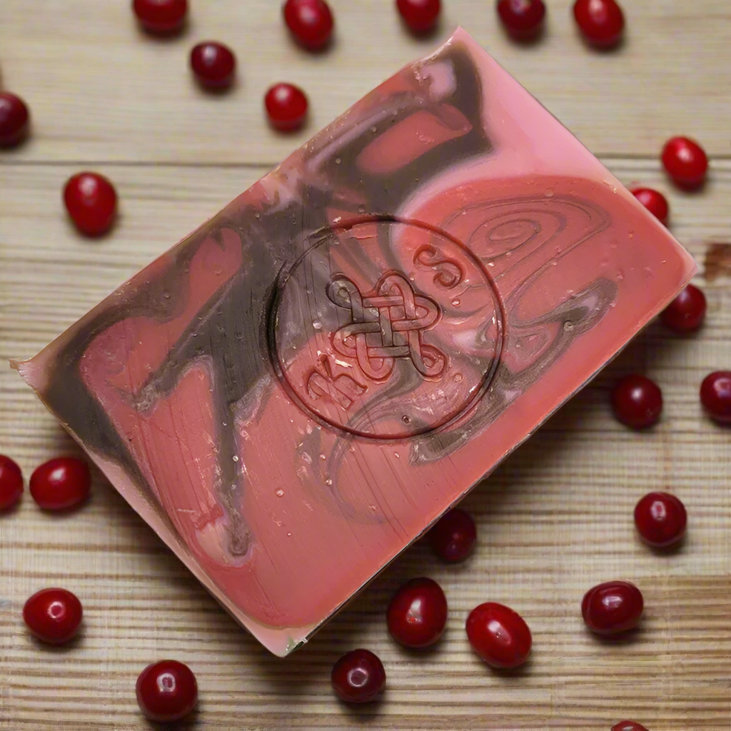 Bar of soap with a brand logo surrounded by red berries on a wooden surface